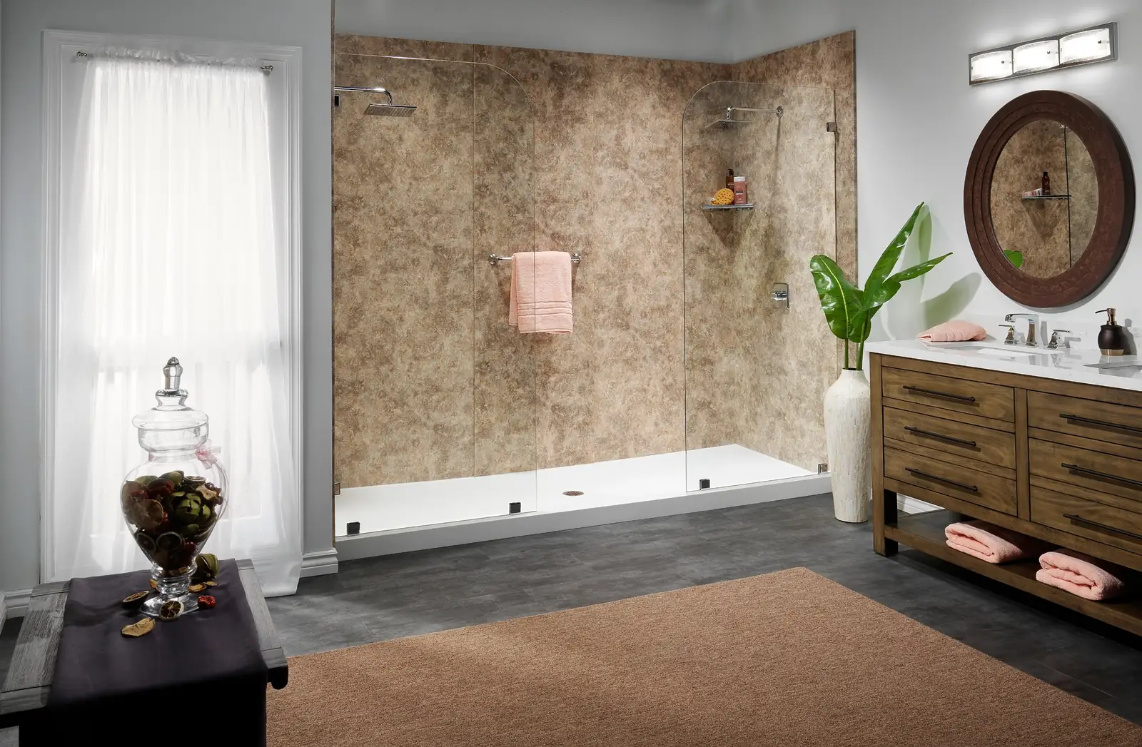Large walk-in shower with tan stone-look wall panels, two rain showerheads and clear glass panels, next to a wood double vanity
