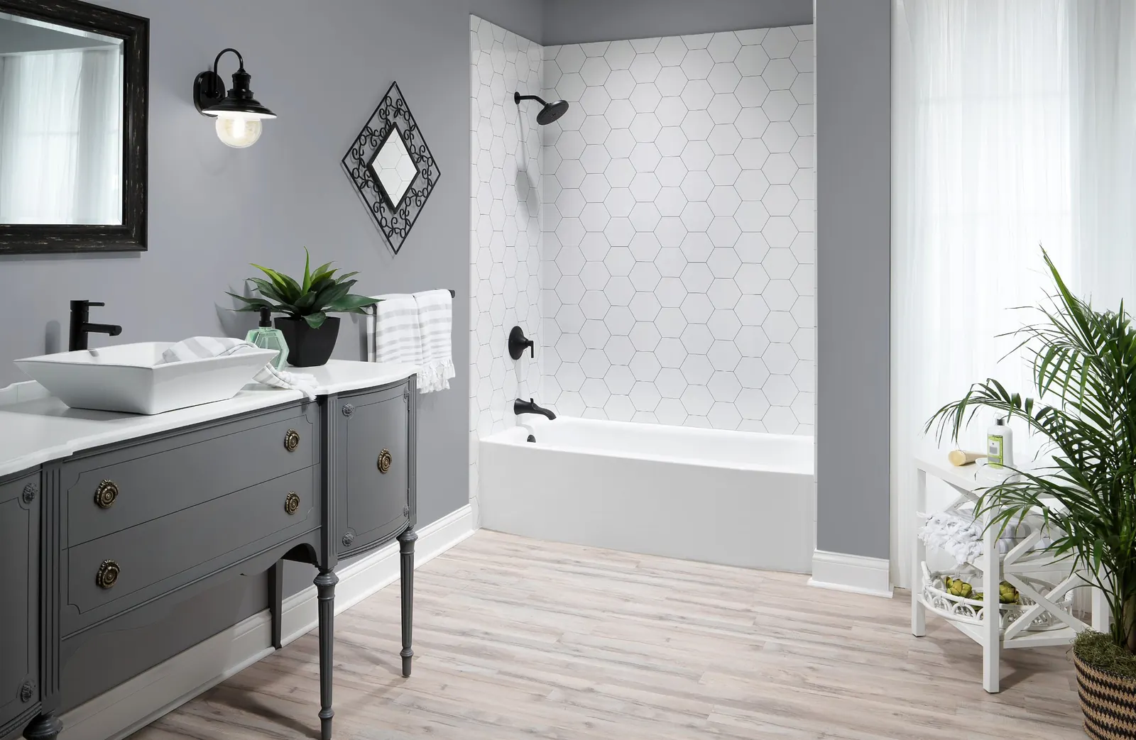 Remodeled bathroom with a white bathtub and white hexagon-pattern wall panels, a gray vanity with a vessel sink and light wood-look floors