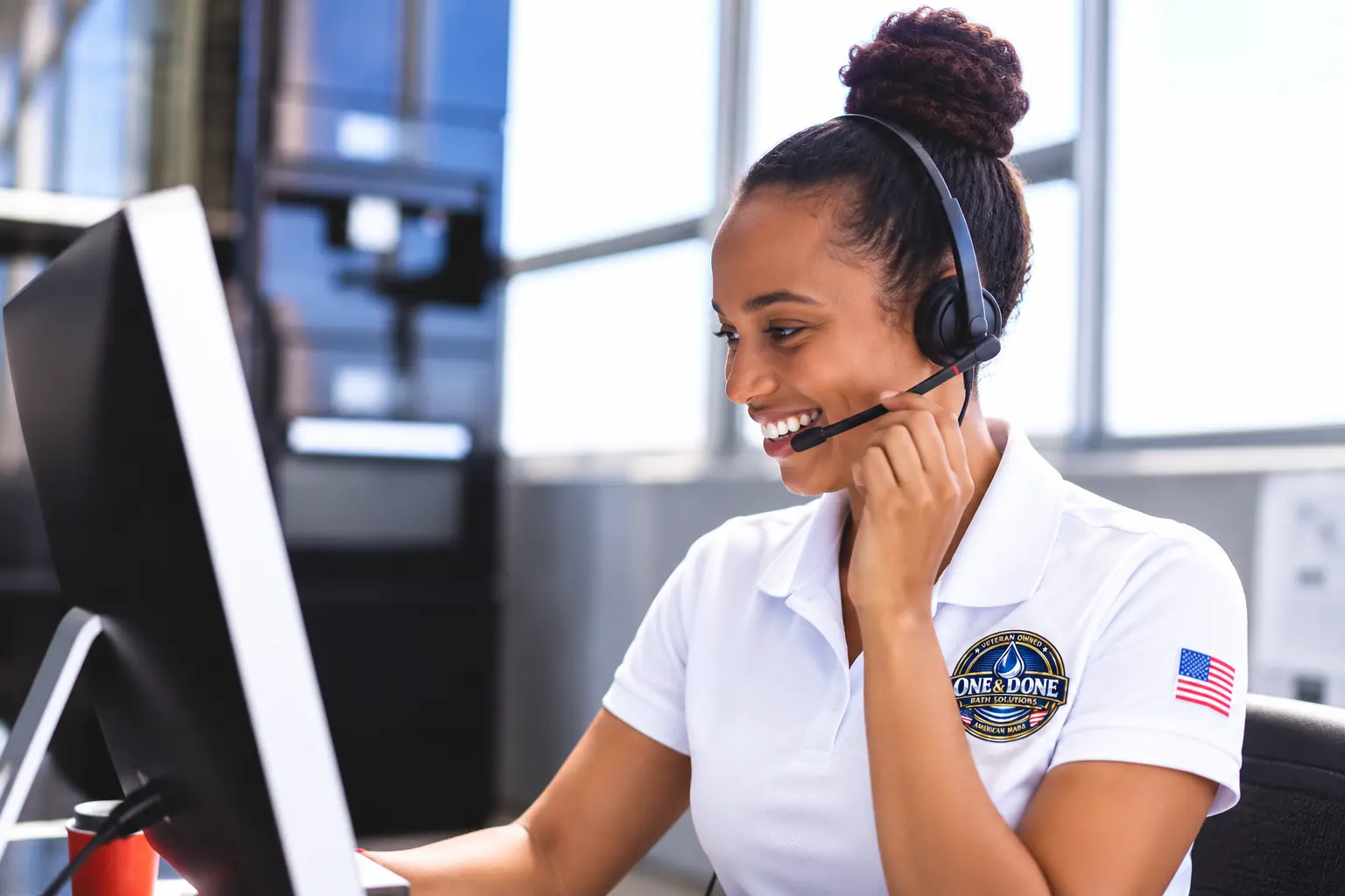 Smiling customer care team member wearing a headset and a One & Done polo, working at a computer