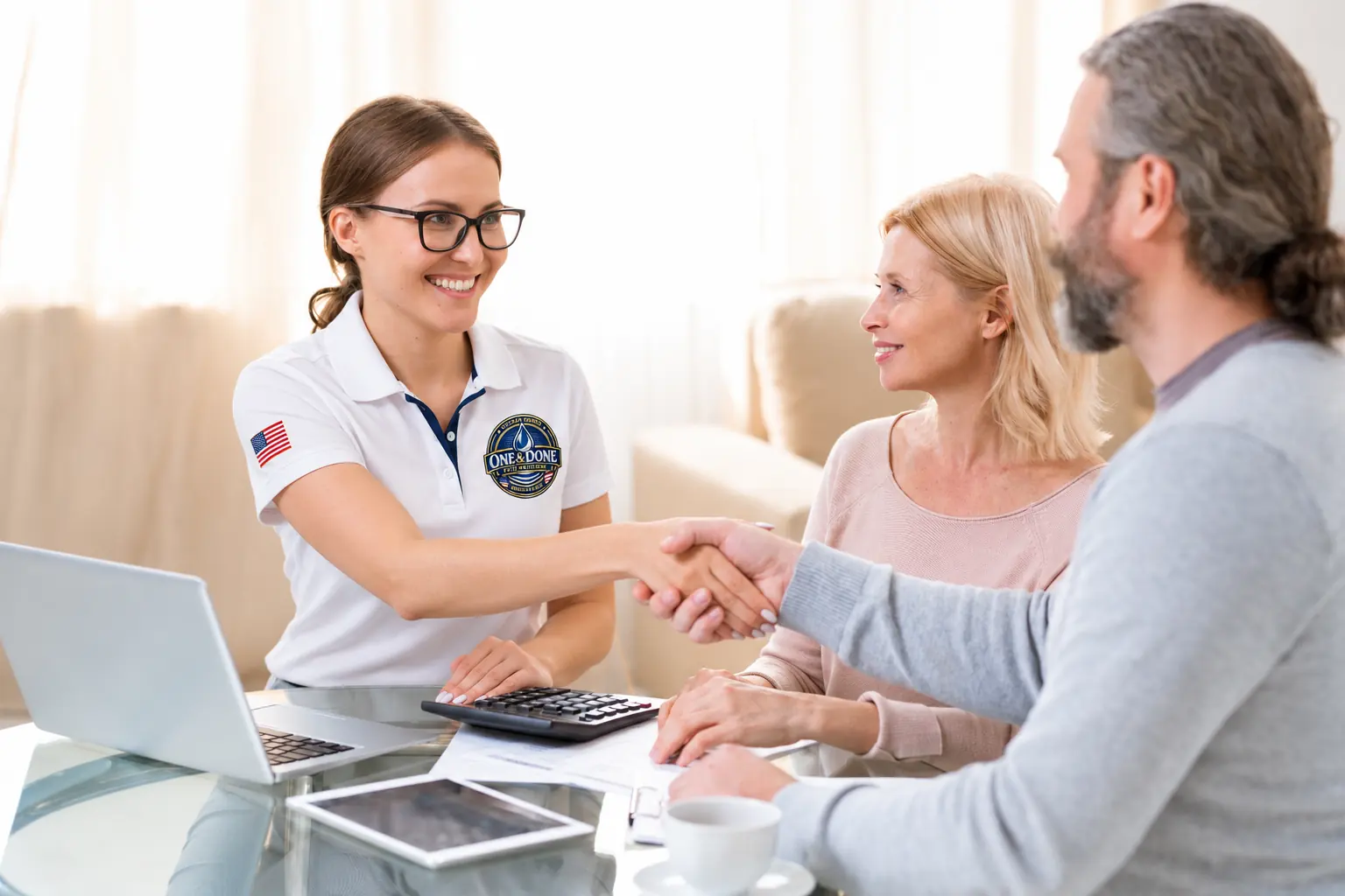 Smiling designer in a One & Done polo shaking hands with a couple at a table during an in-home consultation