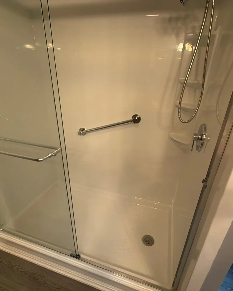 After: new white walk-in shower with a shower base, corner shelves, grab bar and sliding glass door