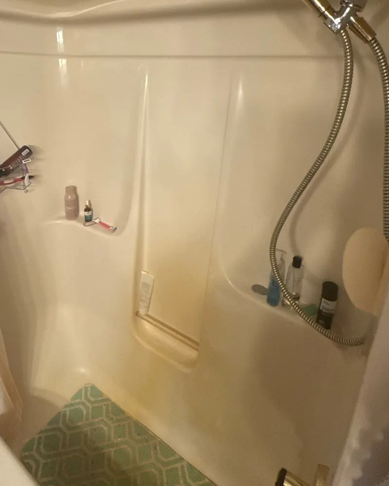 Before: yellowed one-piece tub and shower with a rust-colored stain on the back wall