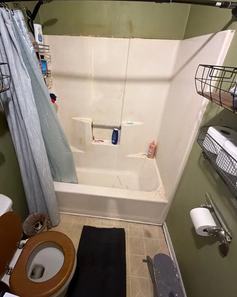Before: stained one-piece fiberglass tub and surround with a shower curtain and wire shelves