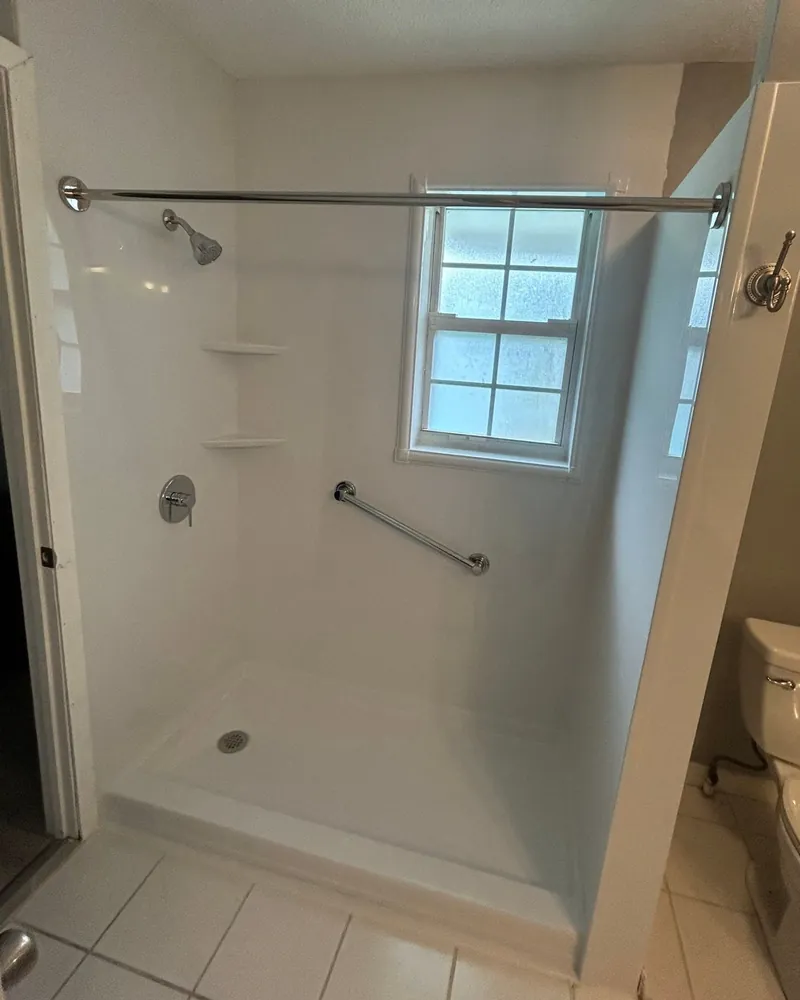 After: new white walk-in shower with a low base, corner shelves, chrome valve, angled grab bar and a window