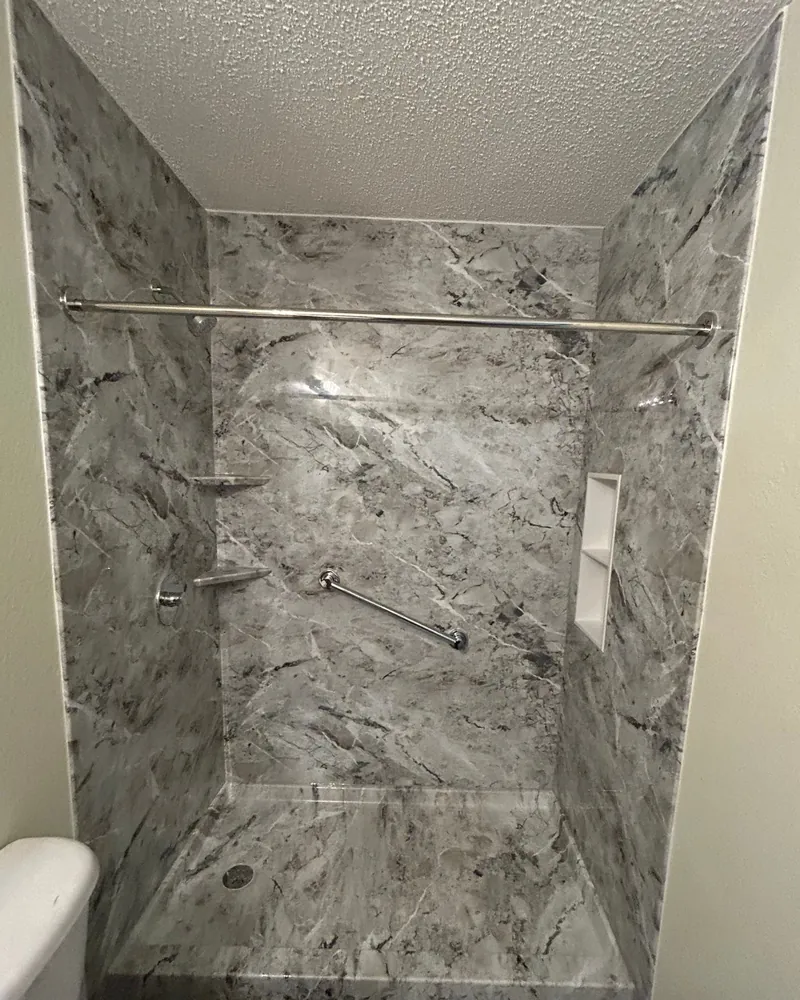 After: walk-in shower with gray marble-look wall panels to the ceiling, a matching shower base, a built-in niche, two corner shelves and a grab bar
