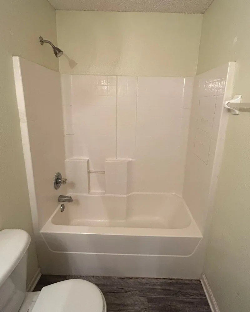 Before: one-piece white fiberglass tub and surround with built-in ledges and a short shower wall