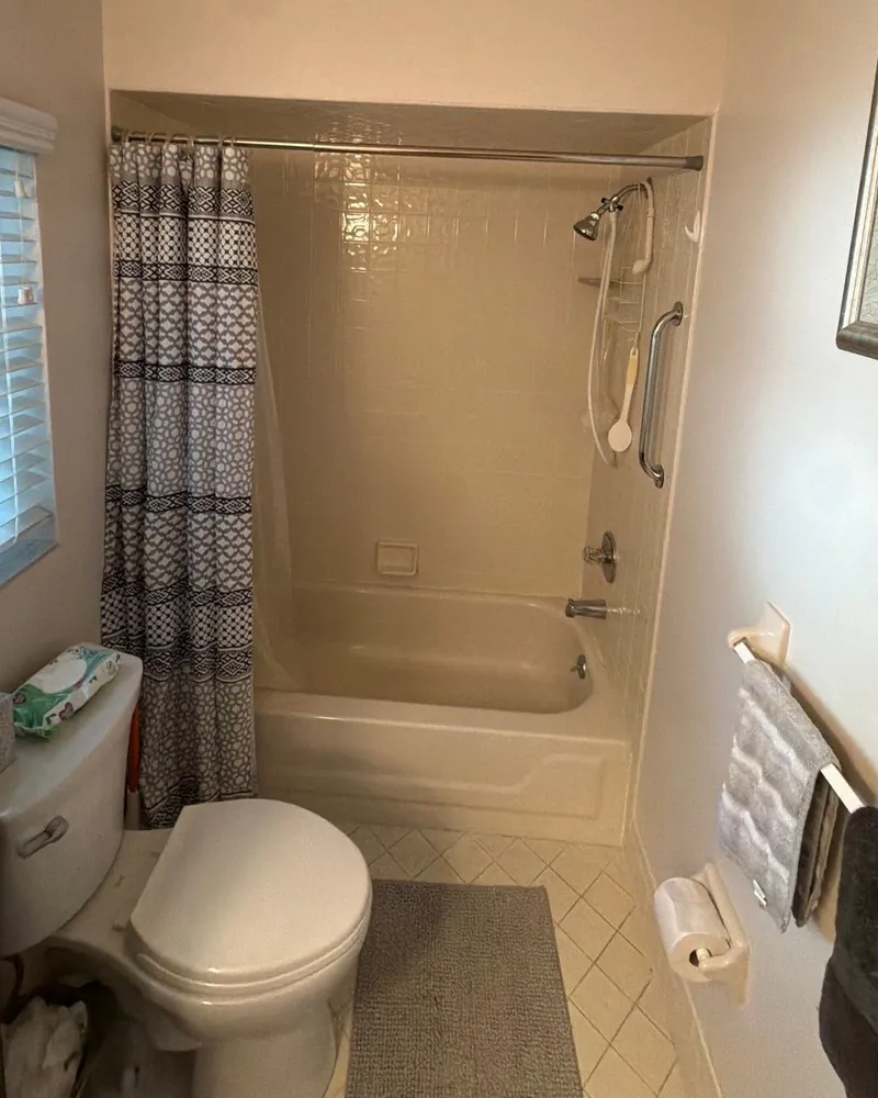 Before: almond tub with a tile surround, a patterned shower curtain and a hand shower on a slide bar