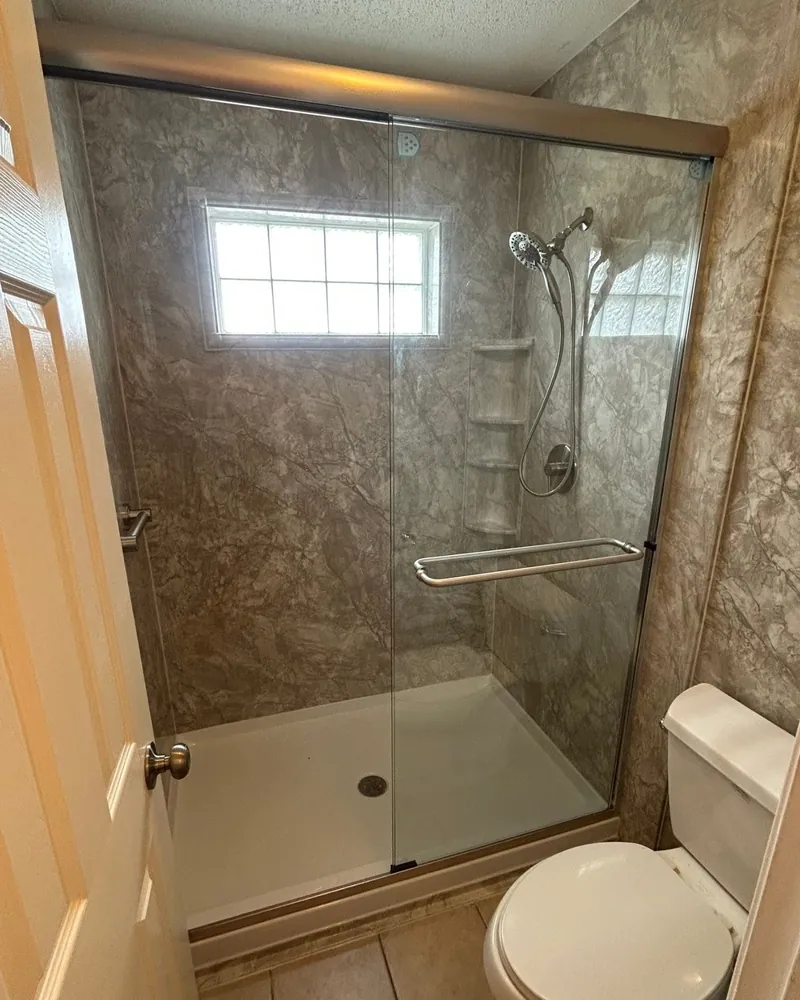After: shower with gray marble-look wall panels, a white shower base, corner shelves, a handheld showerhead and a clear sliding glass door