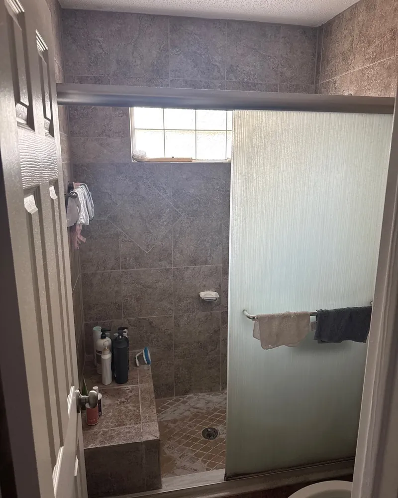 Before: dark tile shower with a tile bench, a tile floor and a frosted sliding glass door