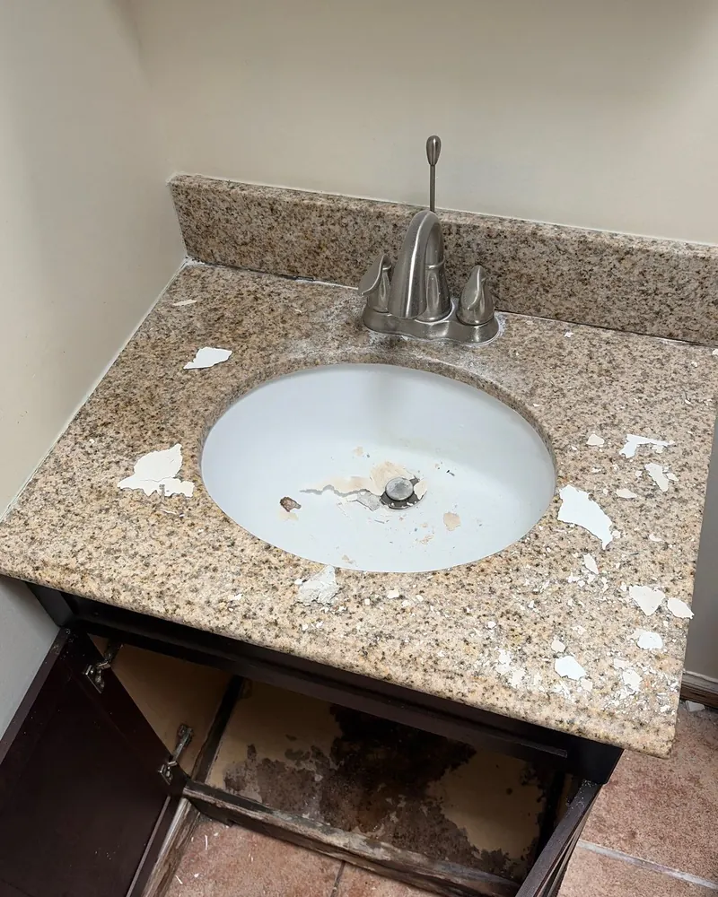 Before: worn vanity with a chipped speckled countertop and a water-damaged cabinet