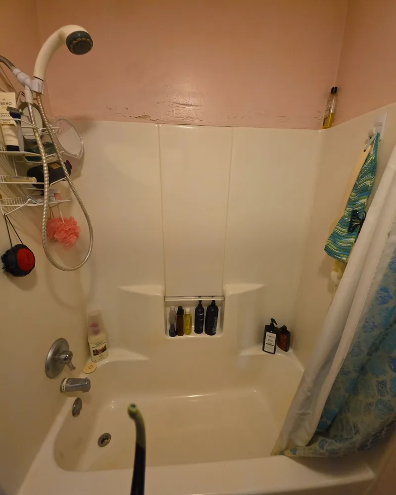 Before: white fiberglass tub and surround with a shower curtain and a peeling wall above it