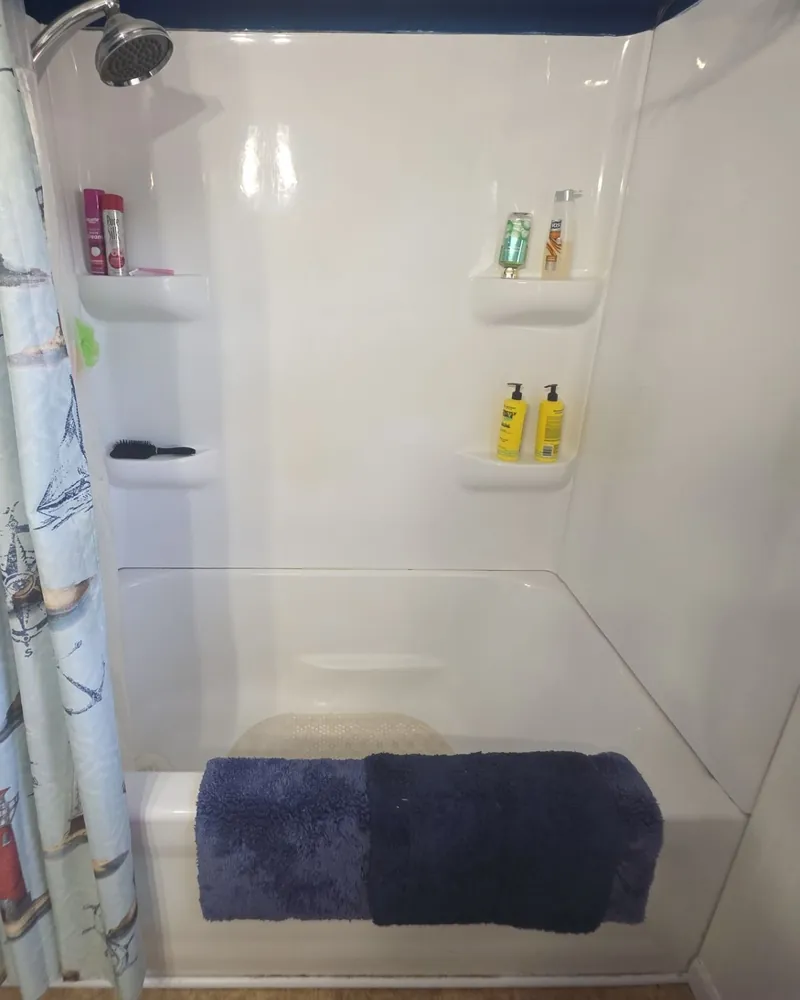 Before: one-piece white fiberglass tub and surround with molded shelves and a shower curtain