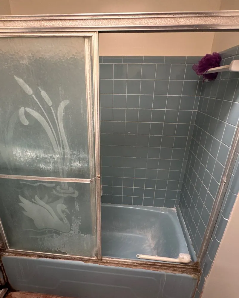 Before: old blue tile tub with a stained frosted sliding glass door and rusted frame